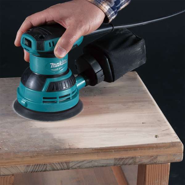 以 Makita 牧田 M9204B 盤式軌道砂光機單手打磨木板表面,機身已接上集塵袋