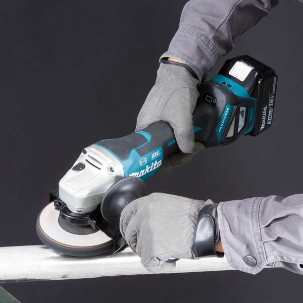 工人戴上手套，使用 Makita DGA518ZU 18V 充電角向磨光機打磨金屬工件