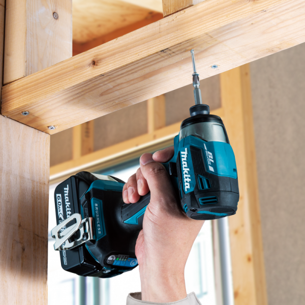 Makita DTD173 cordless impact driver driving a screw overhead in timber framing (blue version shown)