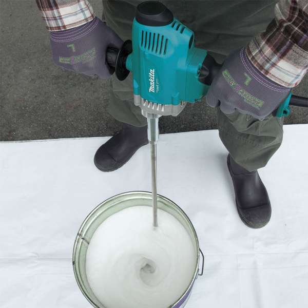 Operator holding the Makita M6600XB power mixer with both hands while mixing paint in a bucket on site