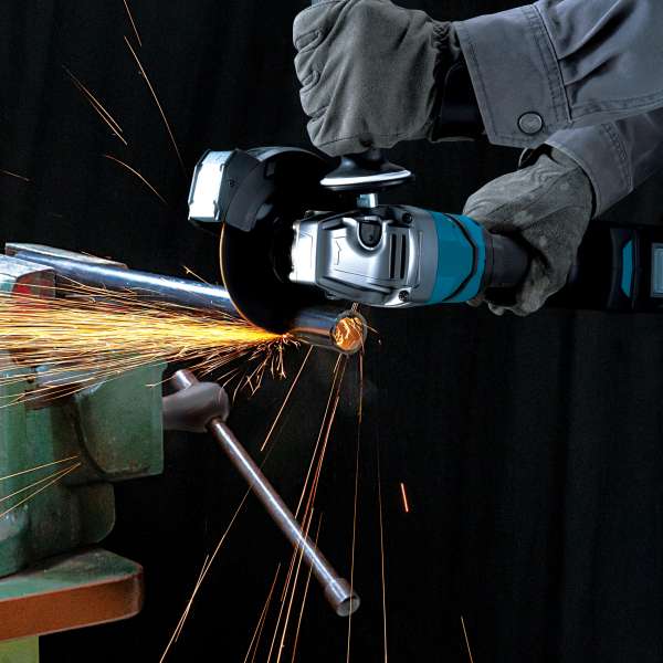 Operator using the Makita GA050GZ cordless angle grinder to grind a metal tube held in a vice, throwing sparks