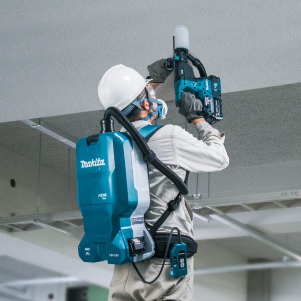 工人手持 Makita 40V 充電式電錘於天花板向上鑽孔，並配合背負式集塵機收集粉塵