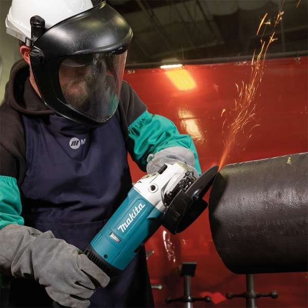 Operator in a face shield grinding a steel pipe with the Makita GA7081 180 mm angle grinder