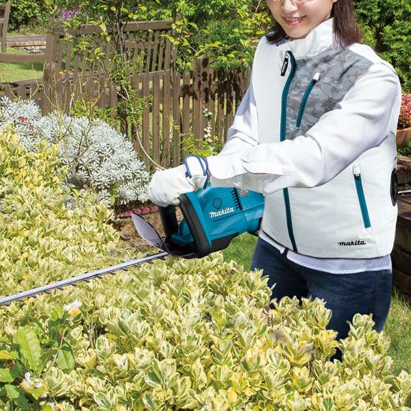 使用者穿著 Makita DFV210AM 充電式冷風背心於戶外花園修剪樹籬