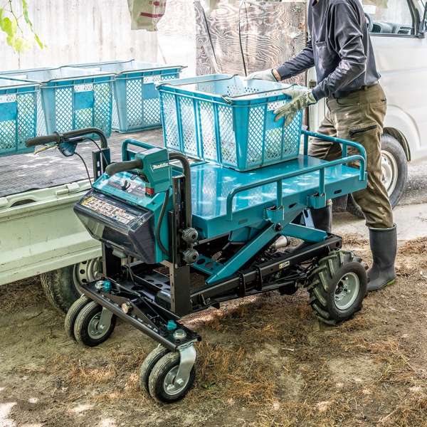 Makita DCU601Z wheelbarrow carrying plastic crates outdoors on a farm beside a truck