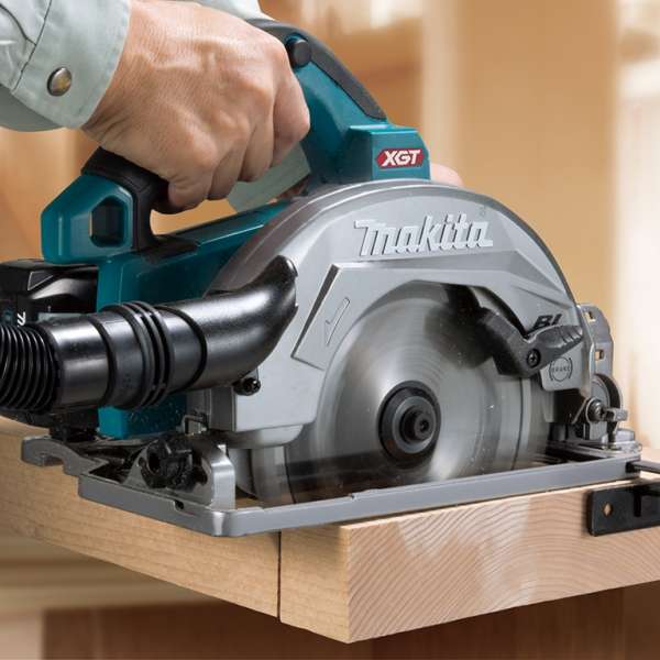 Makita HS004GZ cordless circular saw with dust hose cutting a wooden board
