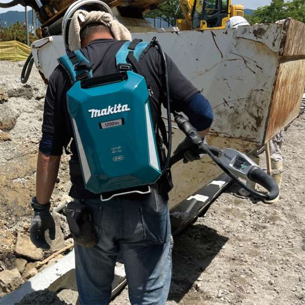 工人背後可見 Makita PDC1200 背負式電池，以電纜連接充電混凝土振盪器作業
