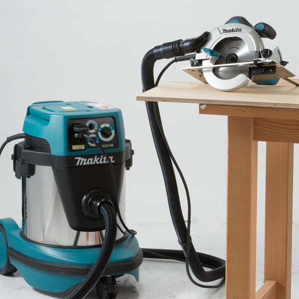 Makita VC2211M vacuum cleaner hose connected to a circular saw cutting on a workbench