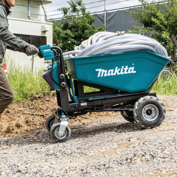 Worker pushing the Makita DCU602Z battery powered wheelbarrow loaded with hoses over gravel