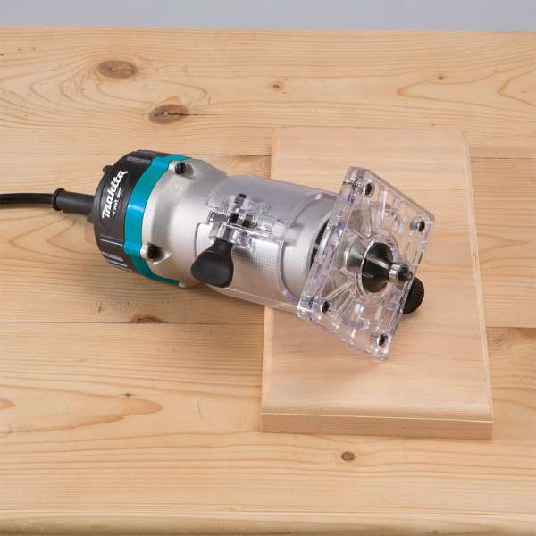 Makita M3701B trimmer resting on a wooden board with its transparent base on the workpiece