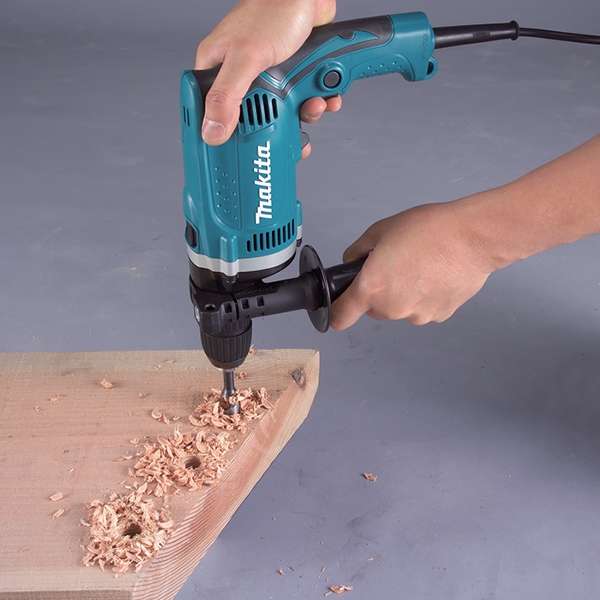 Two-handed operation of the Makita HP1631K hammer drill with side grip drilling into timber