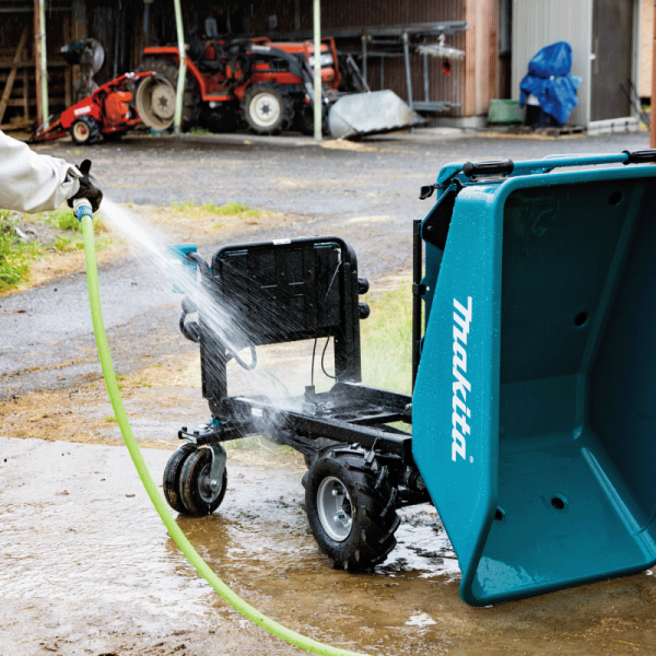 Makita DCU603Z wheelbarrow being hosed down, showing XPT dust and drip resistance