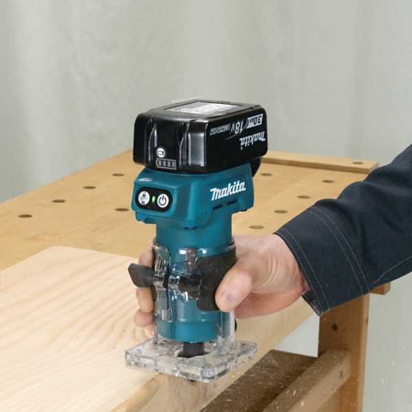Makita DRT52Z 18V 充電式修邊雕刻機單手握持於木材邊緣進行修邊作業