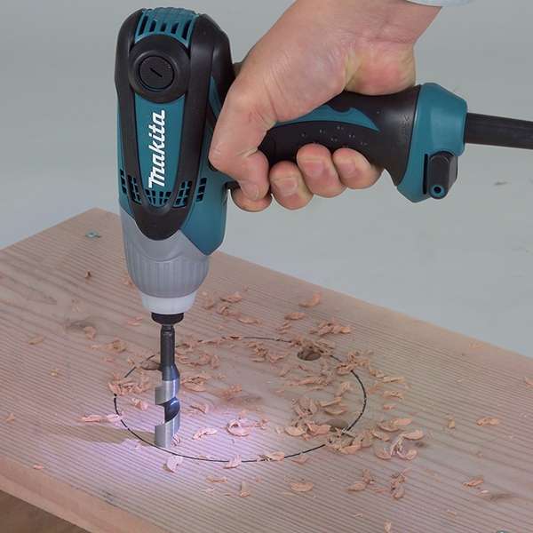 Makita TD0101F impact driver driving a coarse thread screw into a timber board, built-in job light illuminating the work area