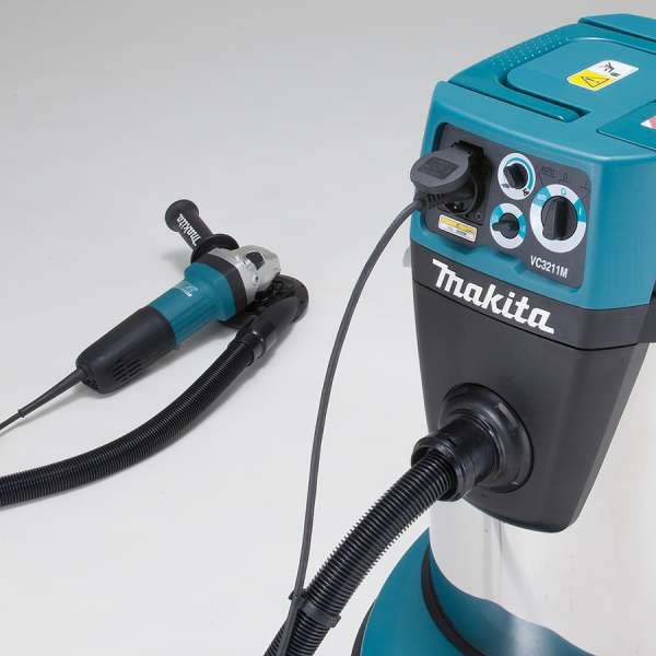 Close-up of the Makita VC3211M control panel with a power tool connected to the on-board socket and hose for dust extraction