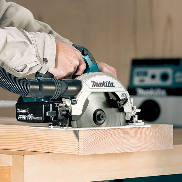 Makita DHS661ZU cordless circular saw with dust hose attached, cutting timber on a workbench