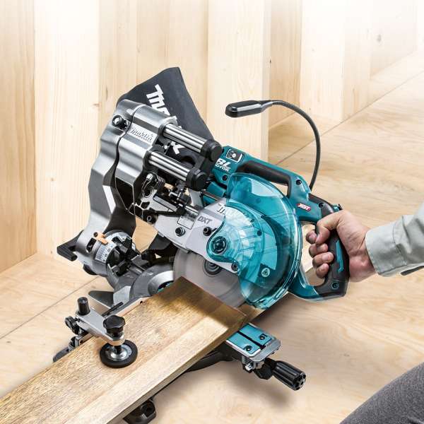 Makita LS001GZ 充電式斜斷鋸貼近木牆擺放，操作員以單手握持手柄切割木板