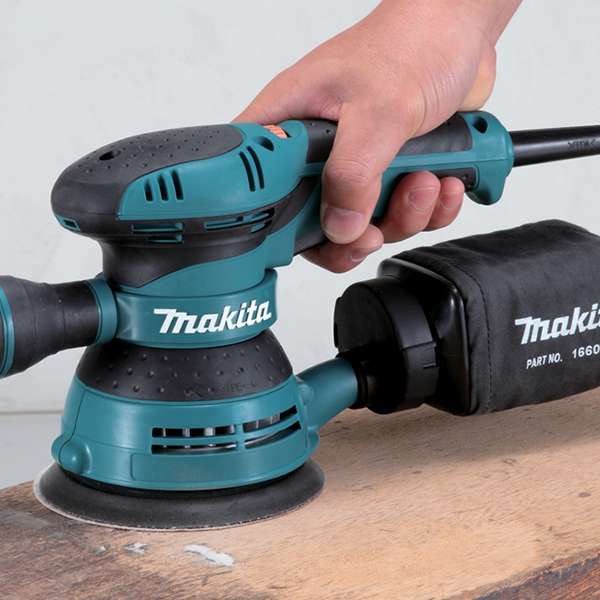 以單手握持 Makita BO5041 平板軌道砂光機並接上集塵袋在木板上打磨