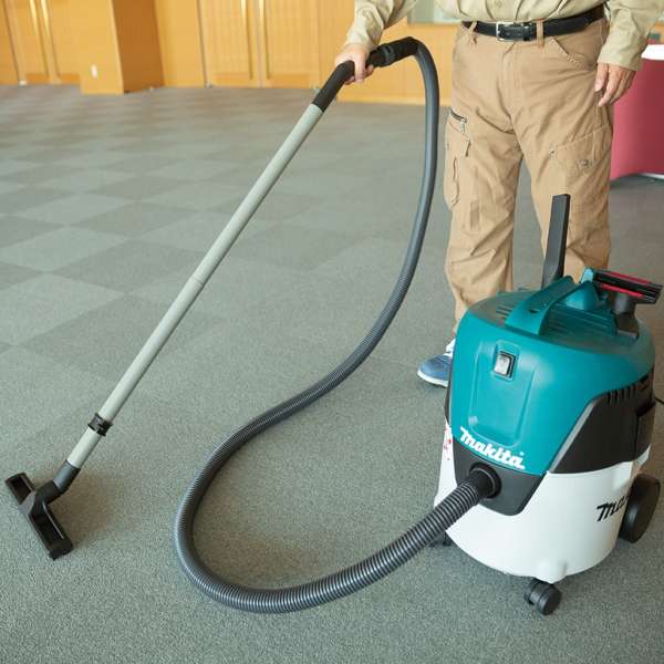 Operator cleaning an indoor floor with the Makita VC2000L 20L wet and dry vacuum cleaner