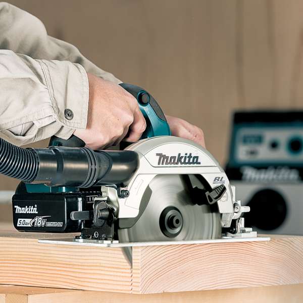 Makita DHS660ZK 18V cordless circular saw cutting timber with a dust extraction hose connected