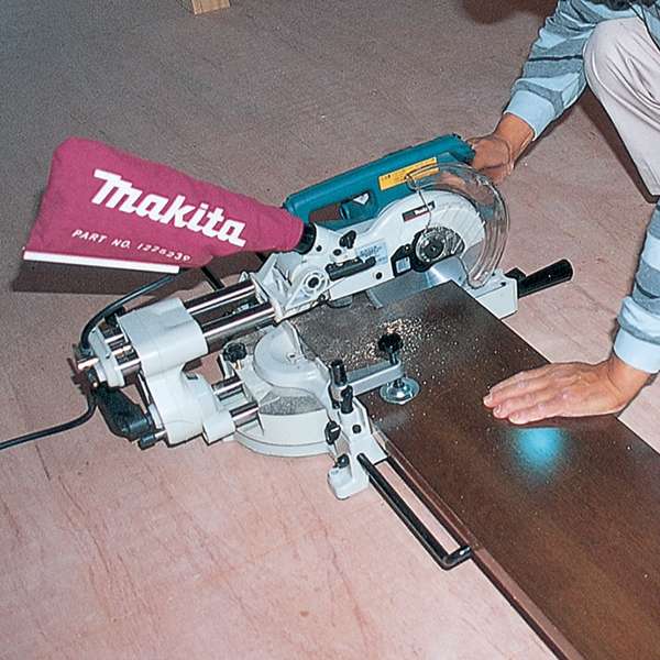 Makita LS0714N slide compound saw cutting a board with the dust bag fitted at the rear
