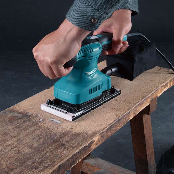 工匠雙手握持 Makita M9203B 平板砂光機於木工檯上打磨木板