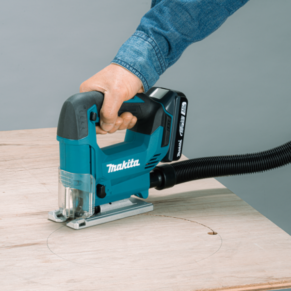 Makita DJV186Z 18V cordless jig saw connected to a vacuum hose cutting a circle in plywood