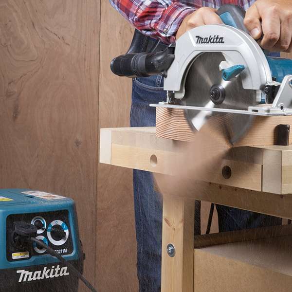 工人在工作台上使用 Makita HS7600 電圓鋸切割木材，並接駁集塵器收集木屑