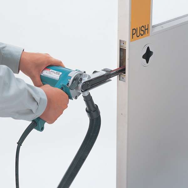 操作員雙手持 Makita 牧田 9032 帶式砂光機，接駁集塵喉管打磨門框金屬鎖位