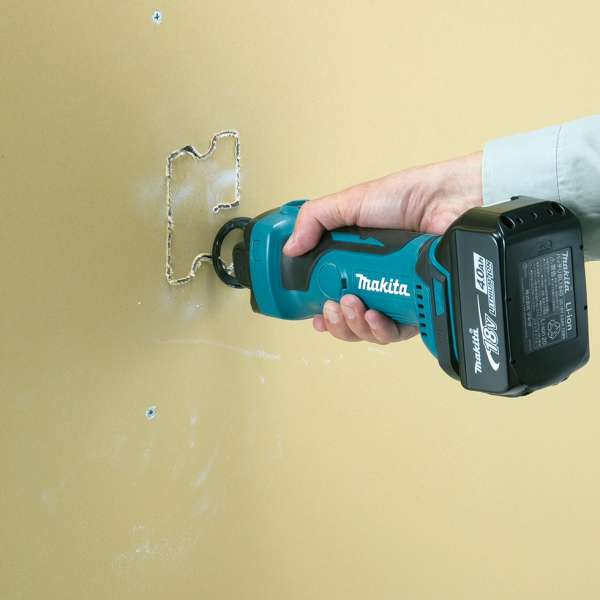 Makita DCO180Z cordless cut-out tool cutting an opening in a gypsum board wall